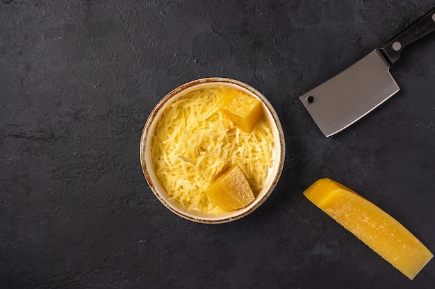 Grated parmesan in ceramic bowl, pieces of cheese and knife