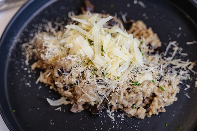 Grated parmesan cheese on top of mushroom risotto on black plate. Healthy vegetarian menu concept