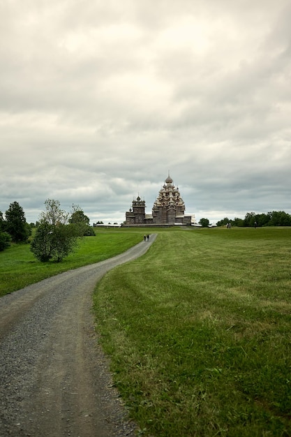 Gravel road leads through a field to a wooden Orthodox church on the island of Kizhi Karelia