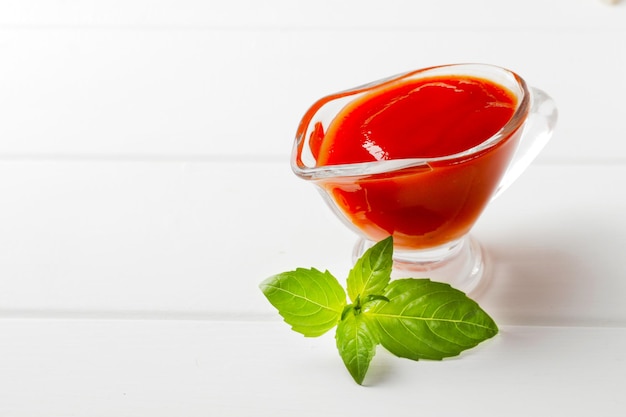 Gravy boat filled with delicious tomato sauce on a white wooden background