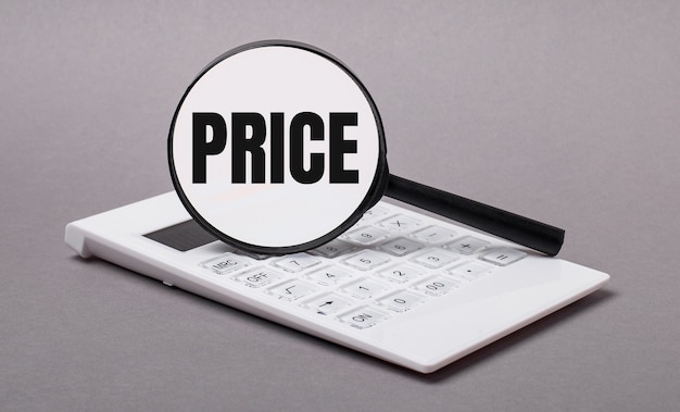 On gray background black calculator and magnifier with text PRICE. Business concept