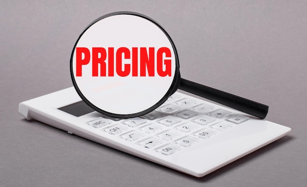 On gray background black calculator and magnifier with text PRICING. Business concept