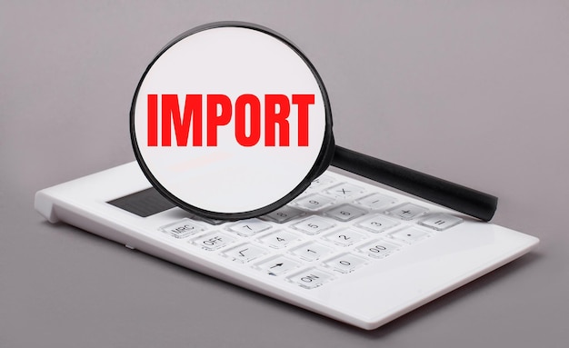 On a gray background a white calculator and a magnifying glass with the text IMPORT Business concept