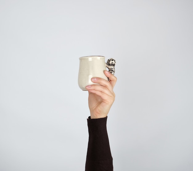 Gray ceramic cup in female hand on a white background, hand raised up