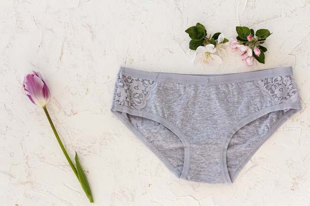 Gray cotton panties with a tulip and flowers of an apple tree on the white structured background. Woman underwear set. Top view.