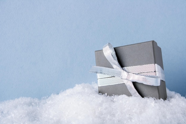 A gray gift box tied with a silver ribbon lies on the snow copy space