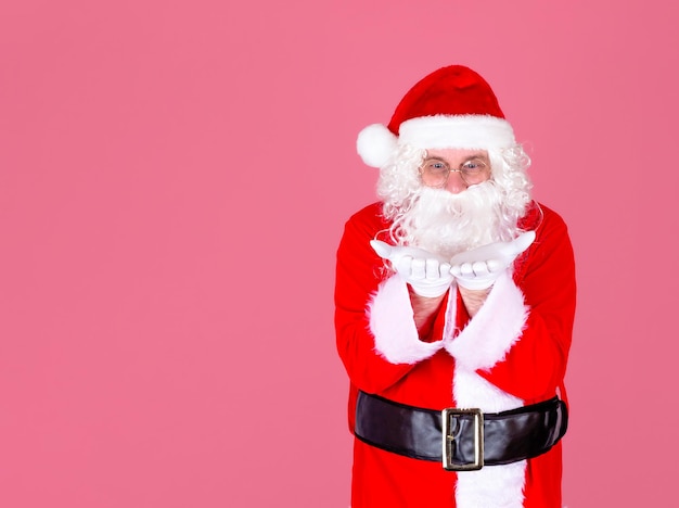 A gray-haired cheerful man in a Santa suit looks at his hands in white gloves