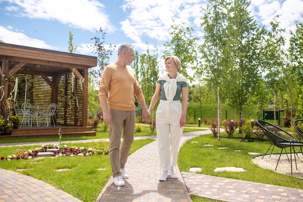 . Gray-haired man and a smiling blonde woman holding hands outdoors