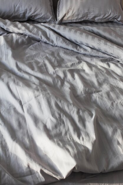 Gray linens in sunlight on bed in bedroom