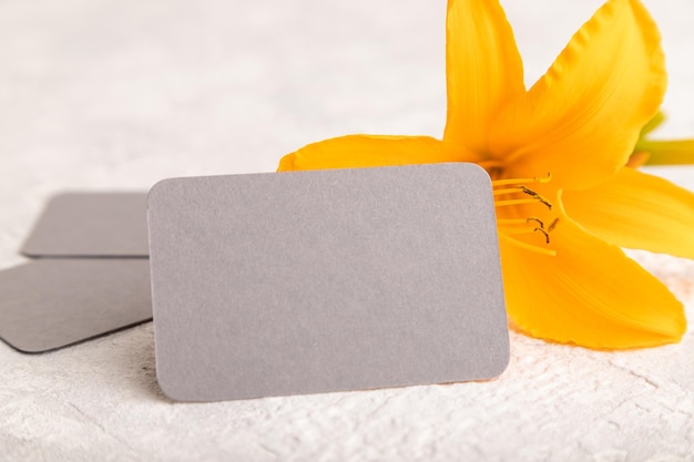 Gray paper business card mockup with orange daylily flower on gray concrete background side view copy space