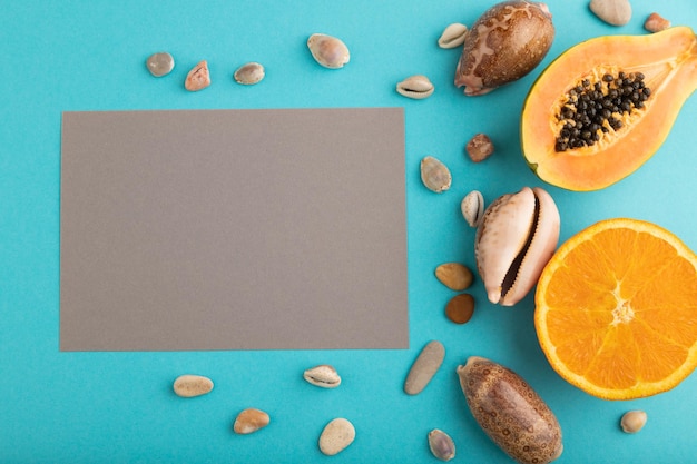 Gray paper business card with ripe cut papaya orange seashells on blue pastel pastel background Top view copy space close up