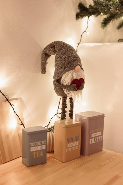 Gray Soft Dwarf On Long Legs Holds Red Heart in his Hands Stands on Wooden Table Among Cans