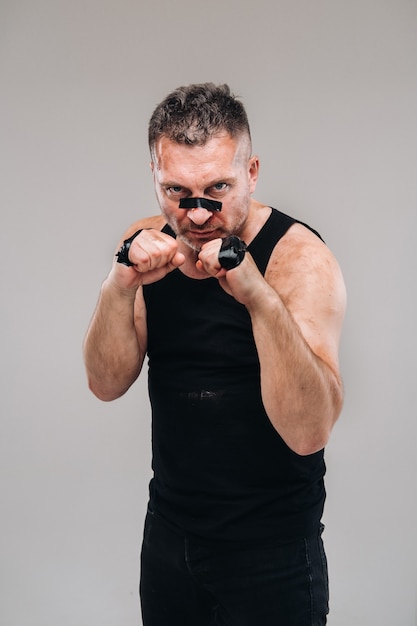 On a gray wall stands a battered man in a black T shirt preparing for a fight.