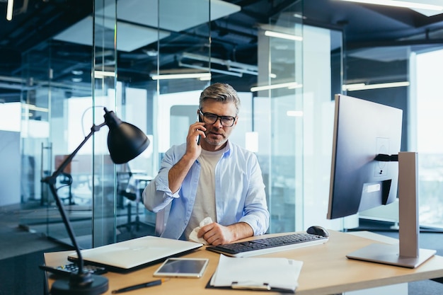 Grayhaired businessman with a runny nose working in the office at the computer cold and flu