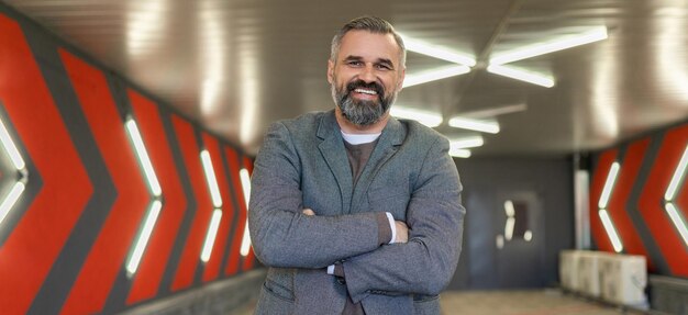 A grayhaired fiftyyearold man businessman in an underground parking lot stands with his arms folded