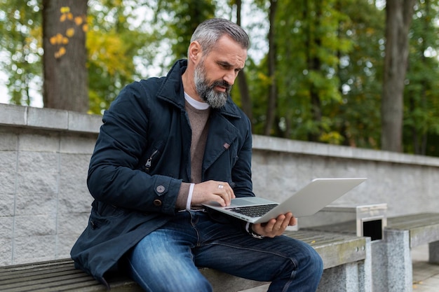 Grayhaired man working on a laptop in the park