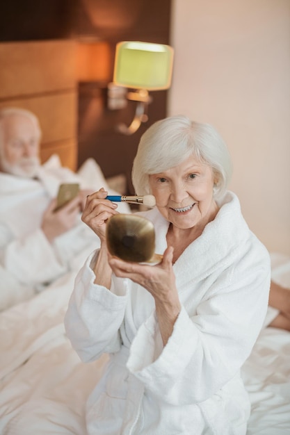 A grayhaired woman doing make up in the morning