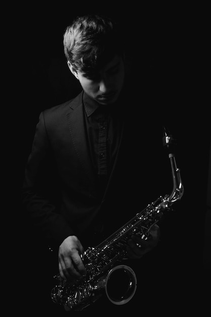 Photo a grayscale shot of a cool and handsome guy holding his saxophone on a dark background