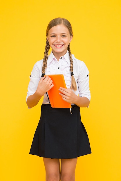 Great book great information Happy little girl holding book with information on yellow background Small child getting information from library book School information