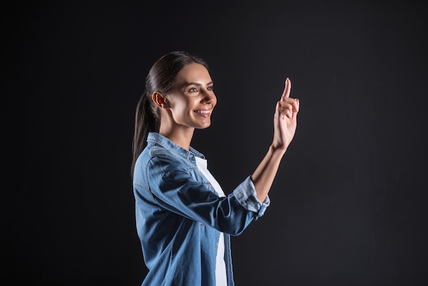 Great mood. Happy delighted positive woman pressing her finger to the sensory screen and smiling while using modern technology