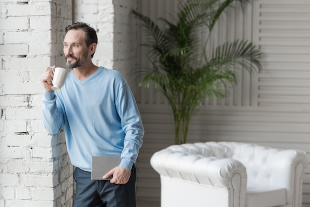 Photo great mood. nice optimistic happy man holding a notebook and drinking coffee while having a good mood