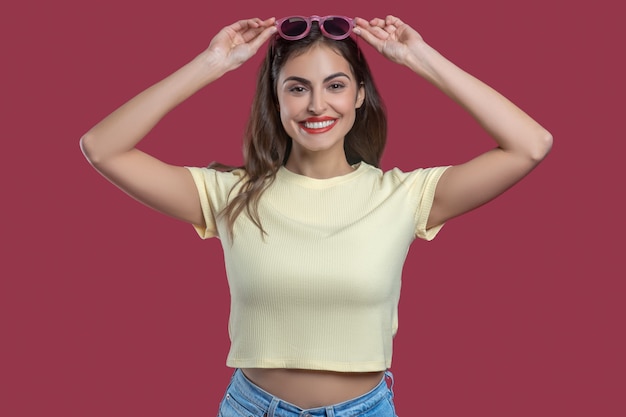 Great mood. Smiling young pretty woman with hands near head holding sunglasses in good mood