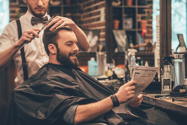 great time at barbershop. cheerful young bearded man getting haircut by hairdresser 