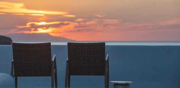 Greece Cyclades Island Two empty woven brown chair opposite blue Aegean sea at sunset