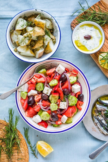 Greek food table scene top view Variety of items including greece salad cucumber dip Tzatziki Anchovy fillets lemon potatoes