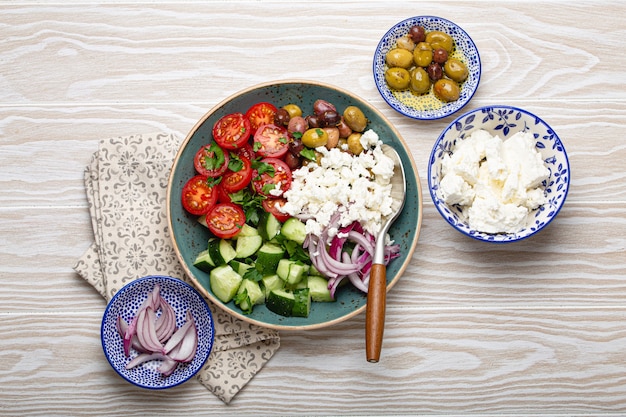 Greek mediterranean salad with tomatoes, feta cheese, cucumber, whole olives and red onion in blue ceramic plate on white wooden background from above, traditional appetizer of Greece