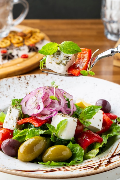 Greek salad with feta cheese, olives and herbs, served in a white plate on a table in a restaurant.