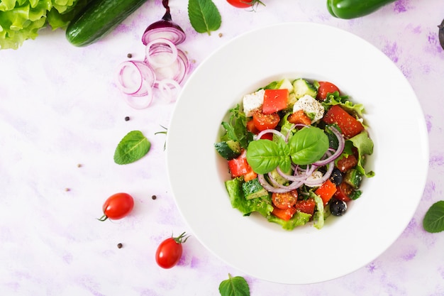 Greek salad with fresh tomato, cucumber, red onion, basil, lettuce, feta cheese, black olives and Italian herbs. Top view