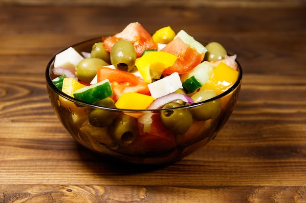 Greek salad with fresh vegetables, feta cheese and green olives in glass bowl on wooden table