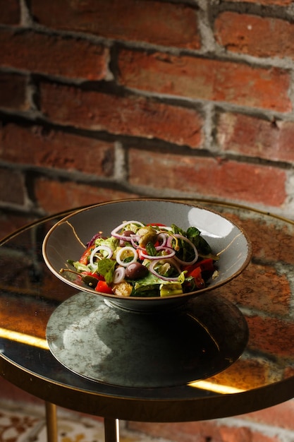 Greek salad with fresh vegetables tomato cucumber red bel pepper lettuce onion olives and cheese Closeup on a white round plate on a wooden background Salad menu with ingredients