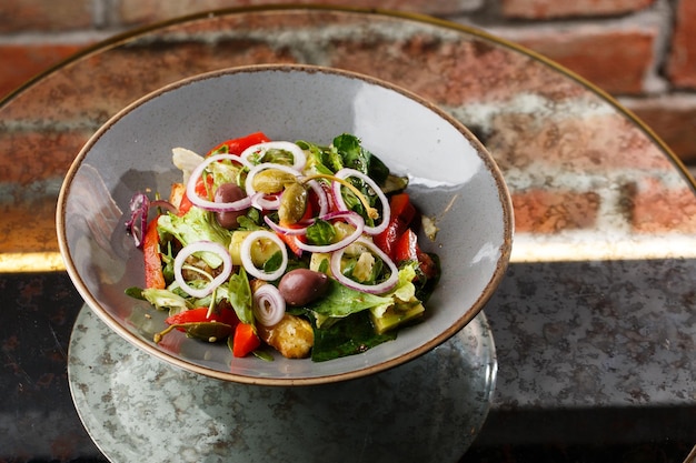 Greek salad with fresh vegetables tomato cucumber red bel pepper lettuce onion olives and cheese Closeup on a white round plate on a wooden background Salad menu with ingredients