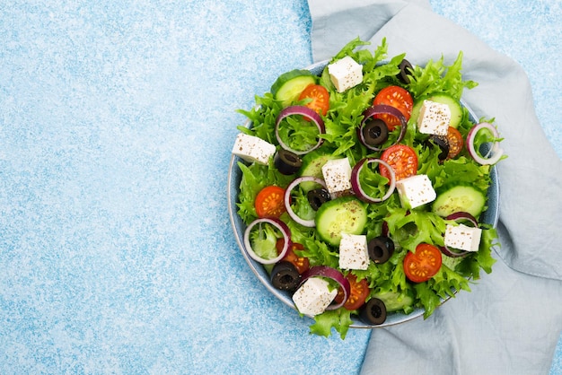 Greek salad with tomatoes, cucumbers, olives and feta cheese in a plate with a napkin on a concrete background, typical Greek cuisine, top view