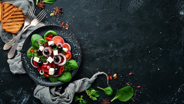 Greek salad with tomatoes paprika onions and feta cheese In a black plate on a wooden background Top view Free space for your text Flat lay