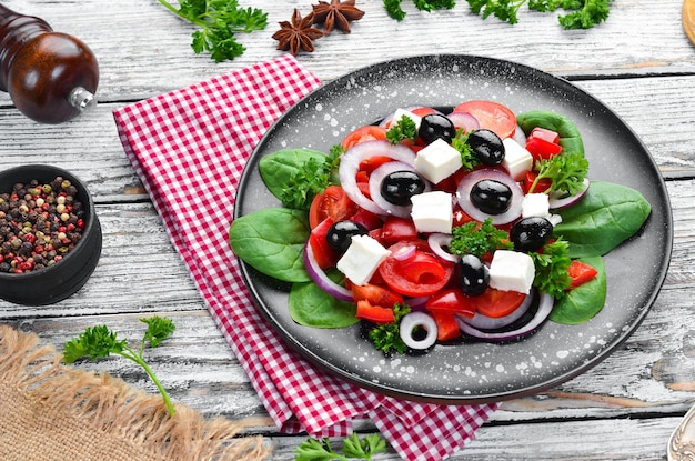 Greek salad with tomatoes paprika onions and feta cheese In a black plate on a wooden background Top view Free space for your text Flat lay