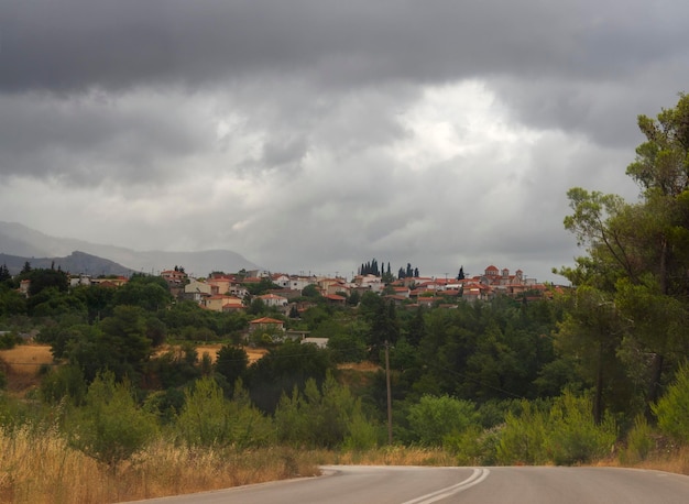 Greek village and Christian Church with bell tower on island Evia in a summer storm with black cloud