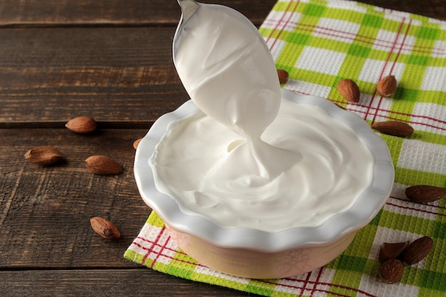 Greek yogurt in a ceramic bowl and with almond nut next to a spoon on a brown wooden background