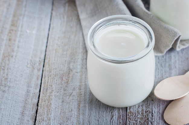 Greek yogurt in a glass jars with wooden spoons on wooden background