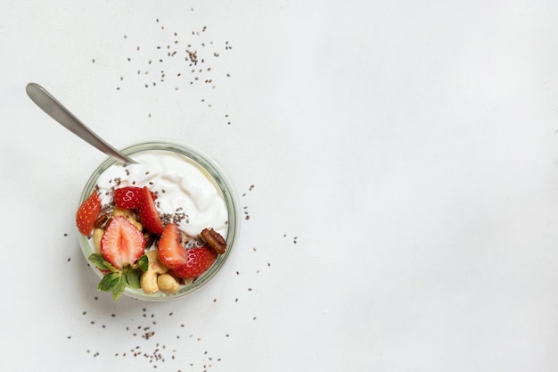 Greek yogurt nuts and strawberries in a glass jar with a spoon on a white table top view