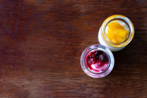 Greek yogurt with berries and mango in glass jars on wooden background