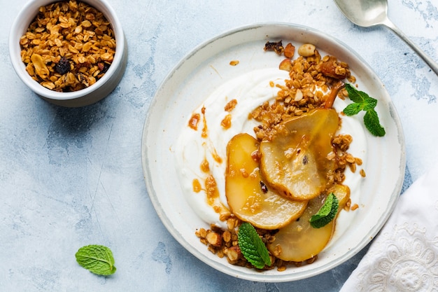 Greek yogurt with caramelized pear, granola, nuts and melted sugar for a wholesome breakfast on a gray ceramic plate. Rustic style. Top view.