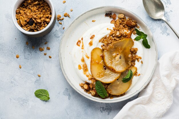 Greek yogurt with caramelized pear, granola, nuts and melted sugar for a wholesome breakfast on a gray ceramic plate. Rustic style. Top view.