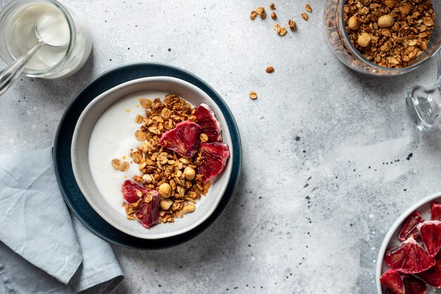 Photo greek yogurt with granola and red orange in a bowl on a gray background