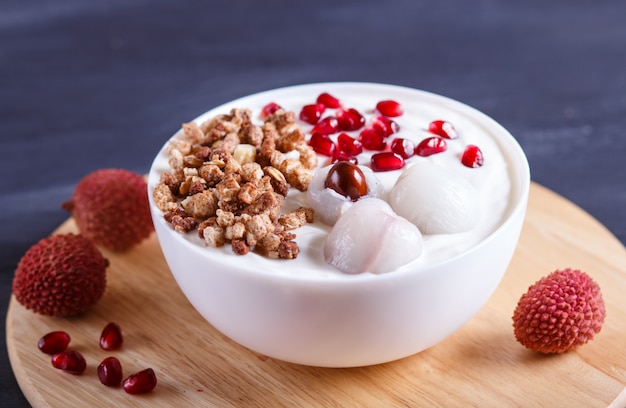 Greek yogurt with lychee, pomegranate seeds and granola in a white plate on a black wooden table