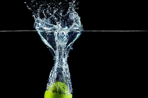 Green apple falling in water with a splash against dark wall close up