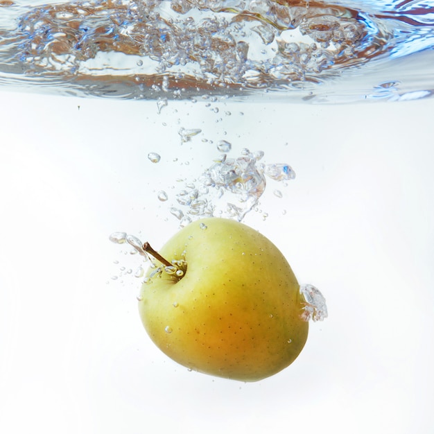 Green apple under water with a trail of transparent bubbles