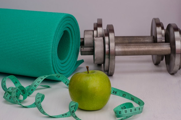 Green apple with dumbbells, a rug and a tape.Female fitness.